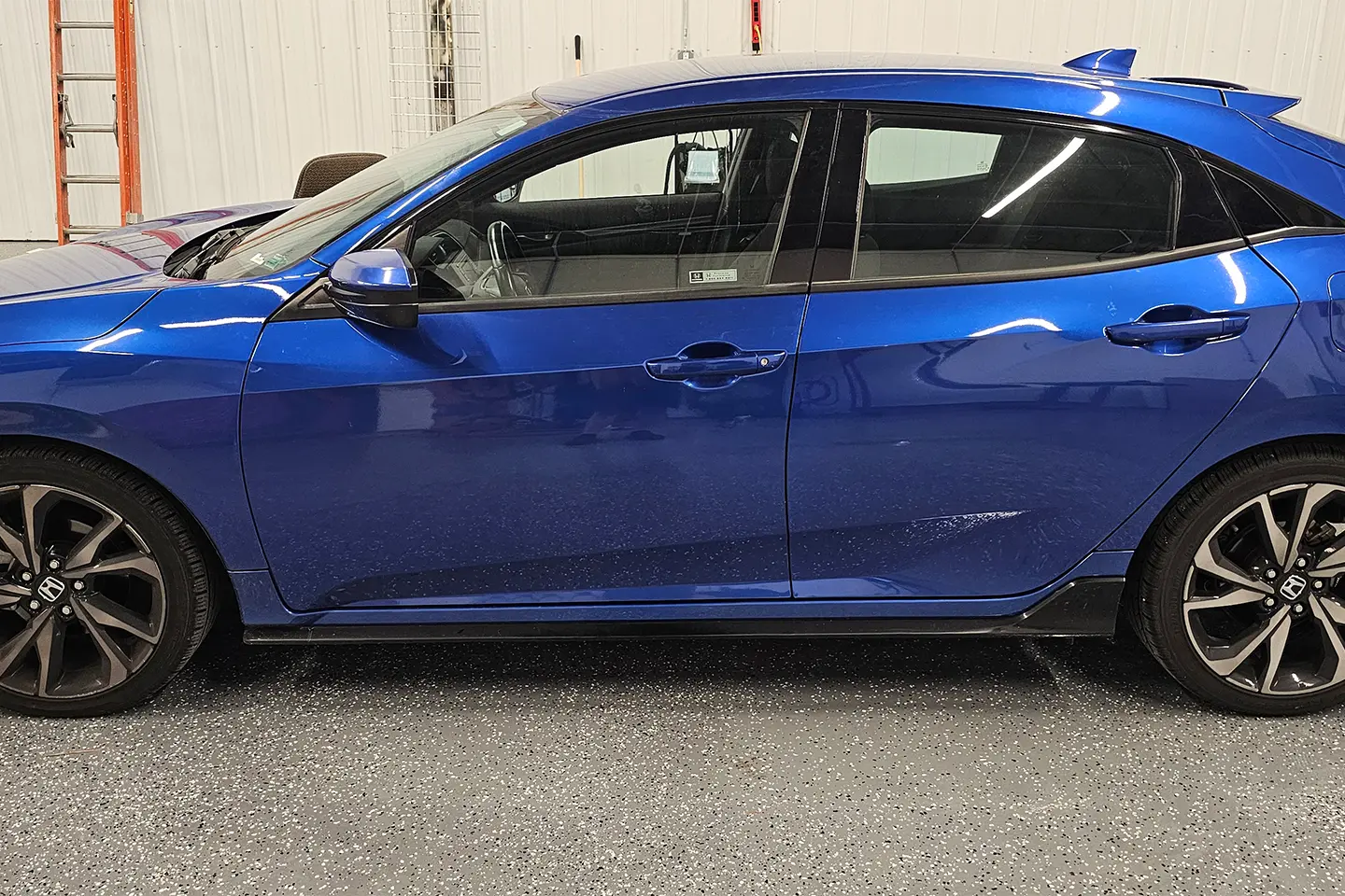 A blue car parked in a parking lot next to a building.